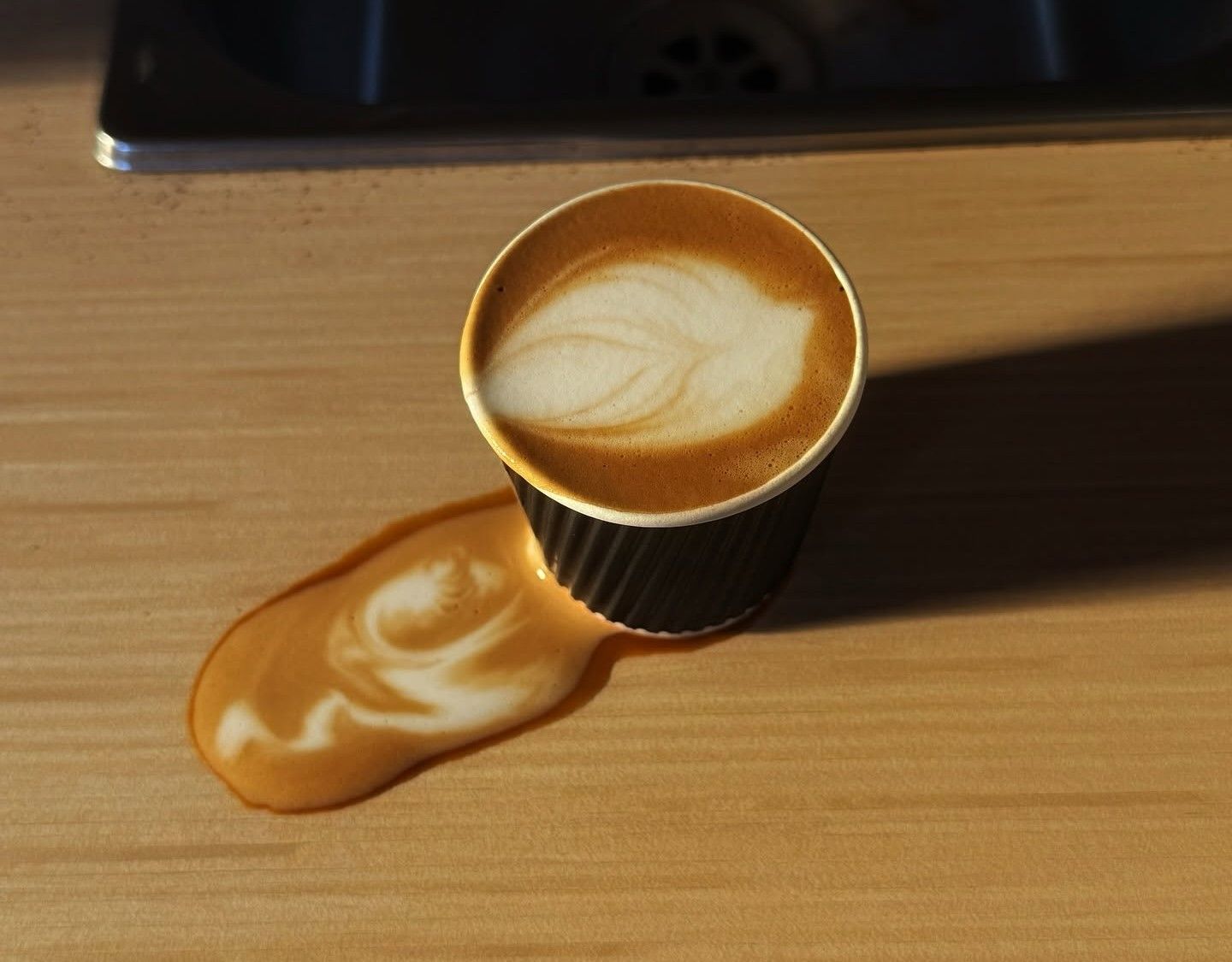 A latte with leaf art beside a spill of espresso crema in warm light at El Cid Coffee